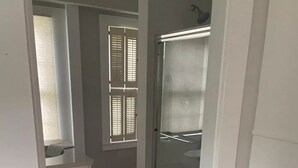 Un pasillo estrecho con suelo de madera, una puerta blanca y una cabina de ducha de vidrio.