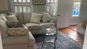 Una sala de estar con un sofá seccional color beige, una mesa de centro de vidrio y una alfombra estampada.