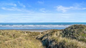 A beach with grassy dunes and a clear blue sky.