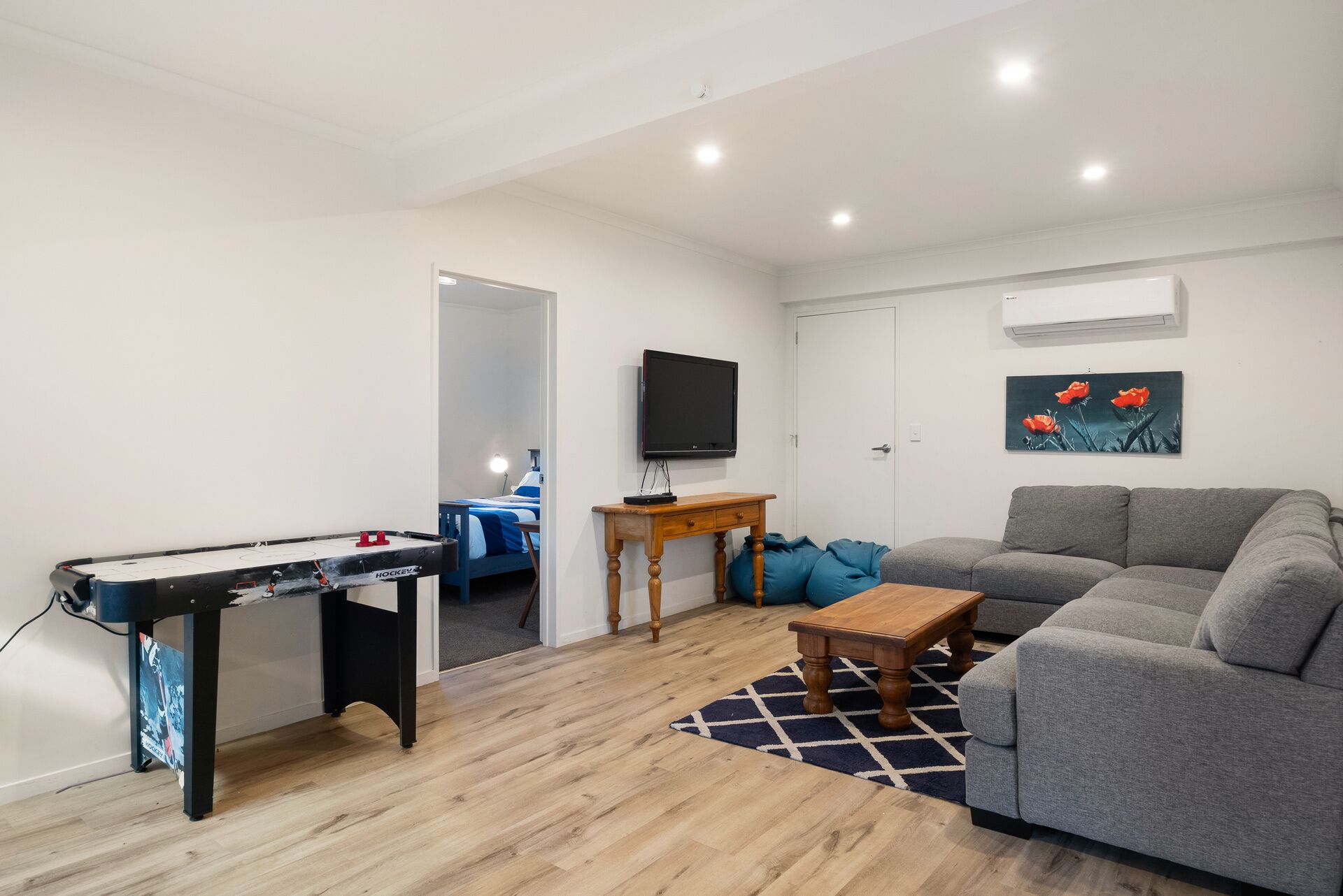 Una sala de estar con mesa de billar, un sofá gris, una mesa de centro de madera y un cuadro en la pared.
