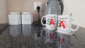 A kitchen counter with a kettle, two coffee mugs, and two coffee containers.