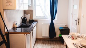 A compact kitchen with a refrigerator, stove, and sink, a window with sheer curtains, and a radiator.