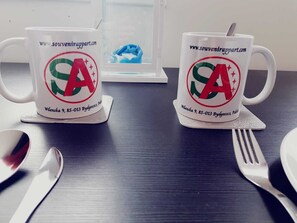 Zwei weiße Tassen mit Logo und Webadresse auf einem dunklen Holztisch.