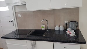 A kitchen with a black countertop, a sink, a kettle, and two mugs.