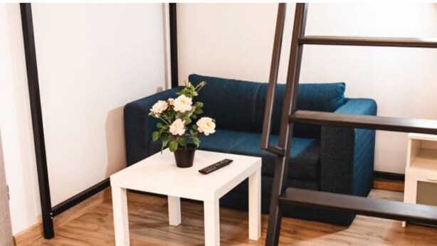 A room with a blue sofa, a white table with a vase of flowers, a ladder, and a small white cabinet.