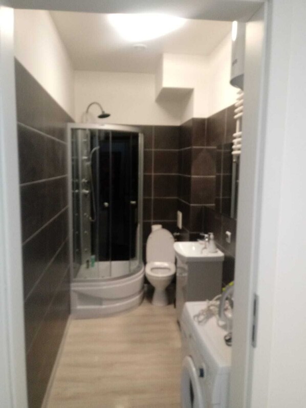 A compact bathroom with a glass shower enclosure, a toilet, and a sink with a mirror.