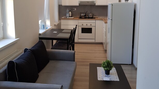 Et moderne køkken med hvide skabe, et spiseområde med sofa og bord, samt en lille potteplante på et sofabord.