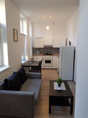 A modern kitchen with white cabinets, a dining area with a sofa and table, and a small potted plant on a coffee table.