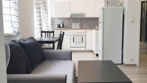 En kompakt opholdsstue med sofa, spisebord, et tekøkken med køleskab og en vaskemaskine.