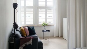 Un salon moderne avec un canapé, une lampe sur pied, une petite table ornée d’un vase de fleurs et un radiateur.