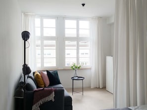 Een moderne woonkamer met een bank, een vloerlamp, een klein tafeltje met een bloevas en een radiator.