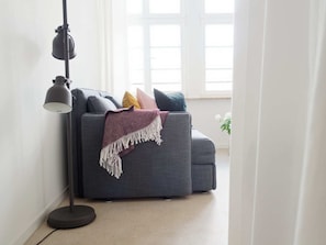 Een moderne woonkamer met een grijze bank, een vloerlamp en een raam met witte gordijnen.