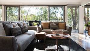 A modern living room with a large sectional sofa, a coffee table, and a view of trees through large windows.