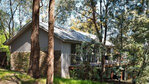 A two-story cabin with a stone foundation, surrounded by trees.