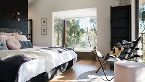 A modern bedroom with a large bed, a window with blinds, a chair, and a wardrobe.