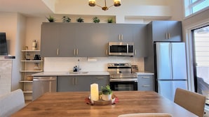Una cocina moderna con armarios grises, electrodomésticos de acero inoxidable y una mesa de madera con cuatro sillas.