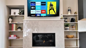 Una sala de estar moderna con chimenea, un televisor montado mostrando servicios de streaming y estanterías con libros y objetos decorativos.