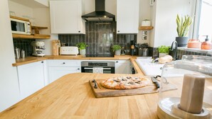 Una cocina moderna con armarios blancos, encimera de madera, una pizza sobre una tabla de cortar y una cafetera.