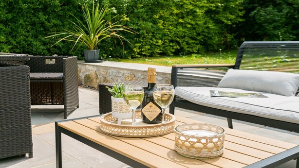 Un espacio al aire libre con mobiliario de mimbre, una bandeja con botellas y vasos, y un candelabro.