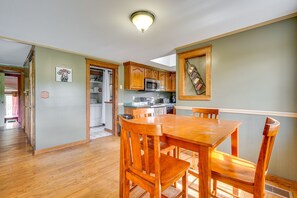 A dining area with a wooden table and chairs, a kitchen with wooden cabinets, and a ceiling light fixture. - Buskirk Vacation Rental w/ Deck & Putting Green! (Buskirk)