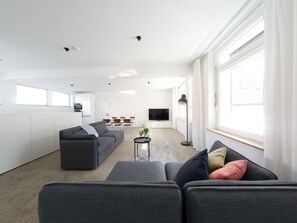Ein modernes Wohnzimmer mit grauem Sofa, Couchtisch und Fernseher im Hintergrund.