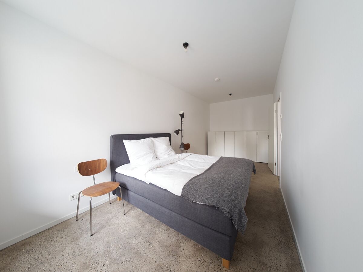 A bedroom with a bed, a chair, and a lamp.