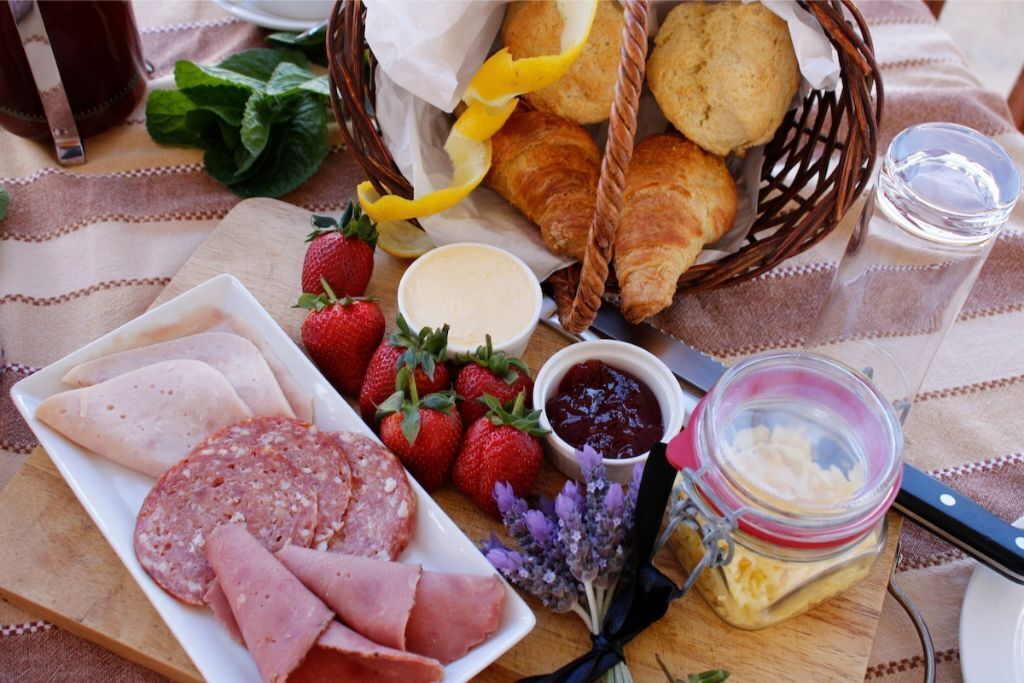 A breakfast spread with croissants, strawberries, ham, and a jar of butter.