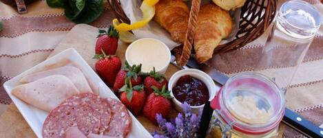 A breakfast spread with croissants, strawberries, ham, and a jar of butter.