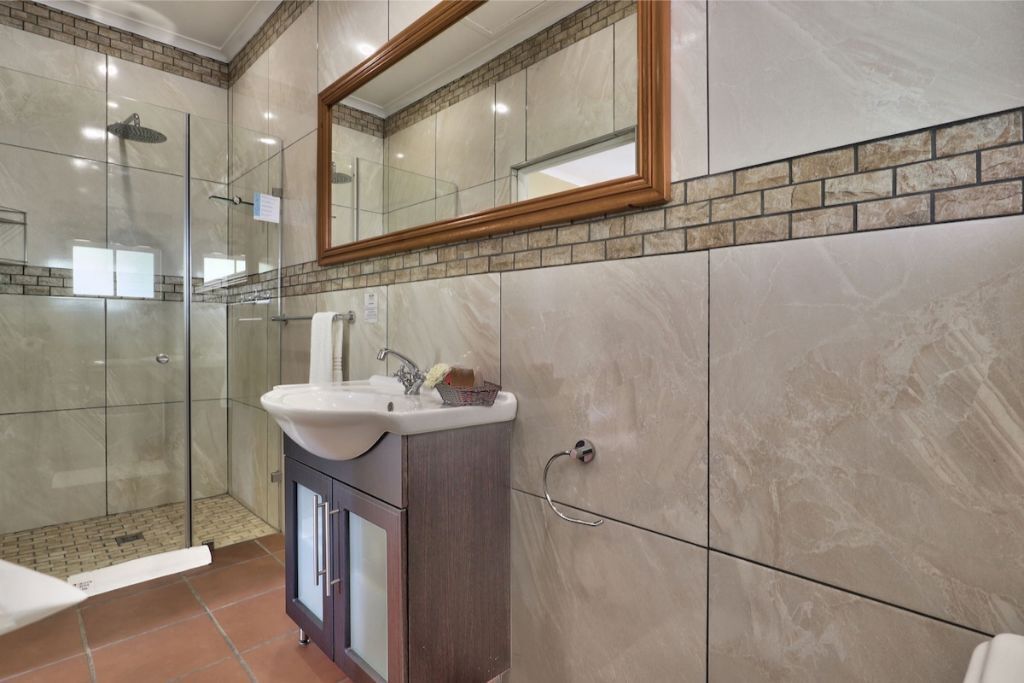 A bathroom with a glass shower enclosure, a sink with a mirror above it, and a tiled wall with a brick accent.