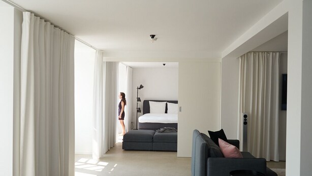 Une chambre d’hôtel moderne avec un grand lit, un canapé gris et une petite table.