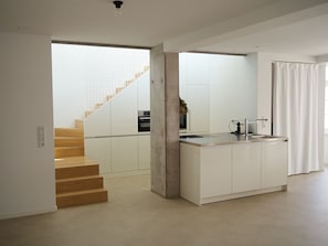 Een moderne keuken met een centraal eiland, een ingebouwde oven en een trap naar een hoger gelegen verdieping.