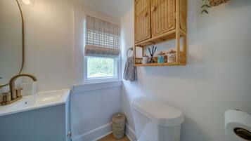 A bathroom with a white sink, a toilet, a window with a blind, and wicker baskets on the wall.