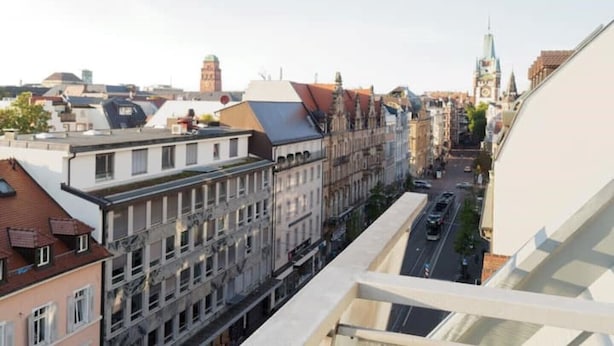 Un paysage urbain comprenant des bâtiments historiques, un imposant beffroi et une construction moderne dotée d’un toit en pente.