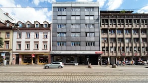 Une vue de rue d’un immeuble moderne, avec des locaux commerciaux au rez-de-chaussée et des logements aux étages supérieurs.