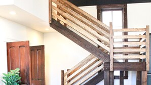 A wooden staircase with a railing, a dining area with a marble table, and a potted plant.