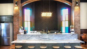 A kitchen with a marble island, bar stools, a stainless steel refrigerator, and a hanging light fixture.