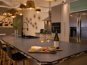 Een moderne keuken met een centraal eiland, roestvrijstalen apparatuur en hangende lampen.