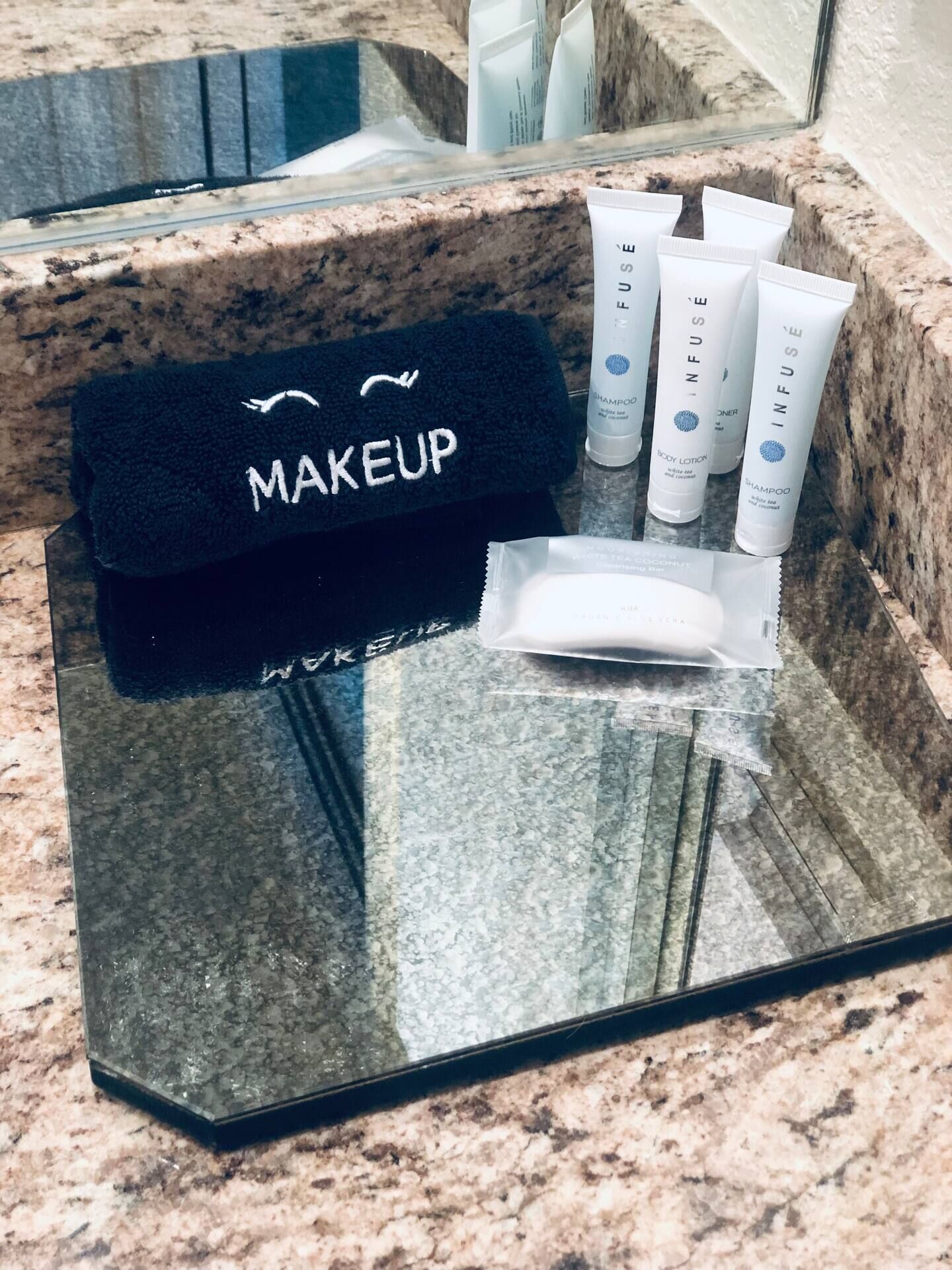 Un tocador de baño con una toalla negra que dice "MAKEUP" y diversos artículos de aseo personal, incluyendo champú, loción corporal y un cepillo de dientes.