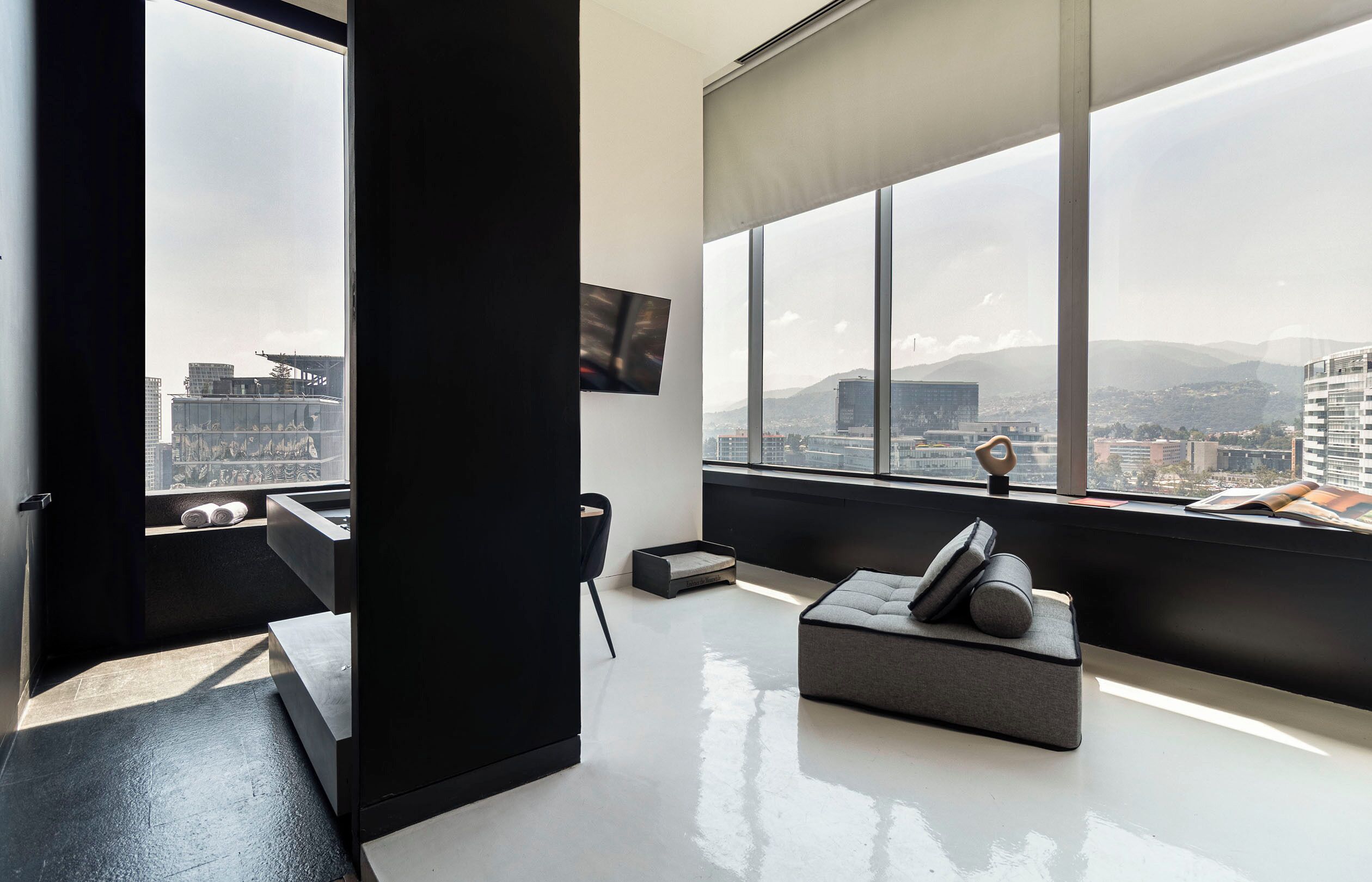 A modern living room with a large window, a flat-screen TV, and a sofa with cushions.