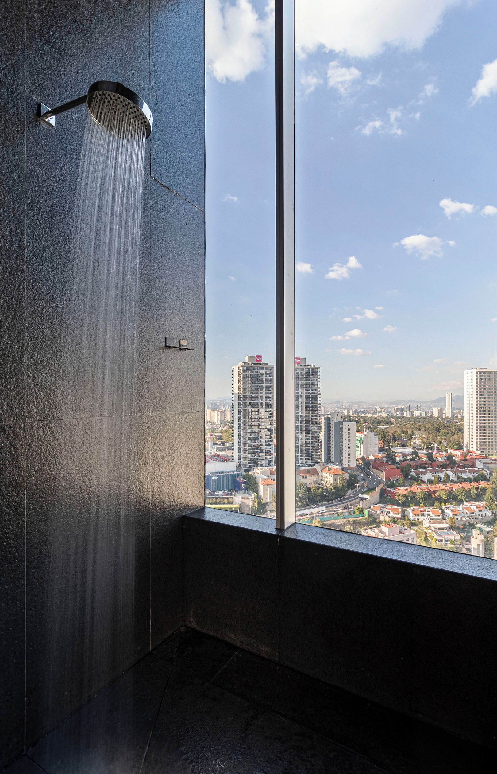 Un baño moderno con un ventanal grande, ducha y vistas a la ciudad.