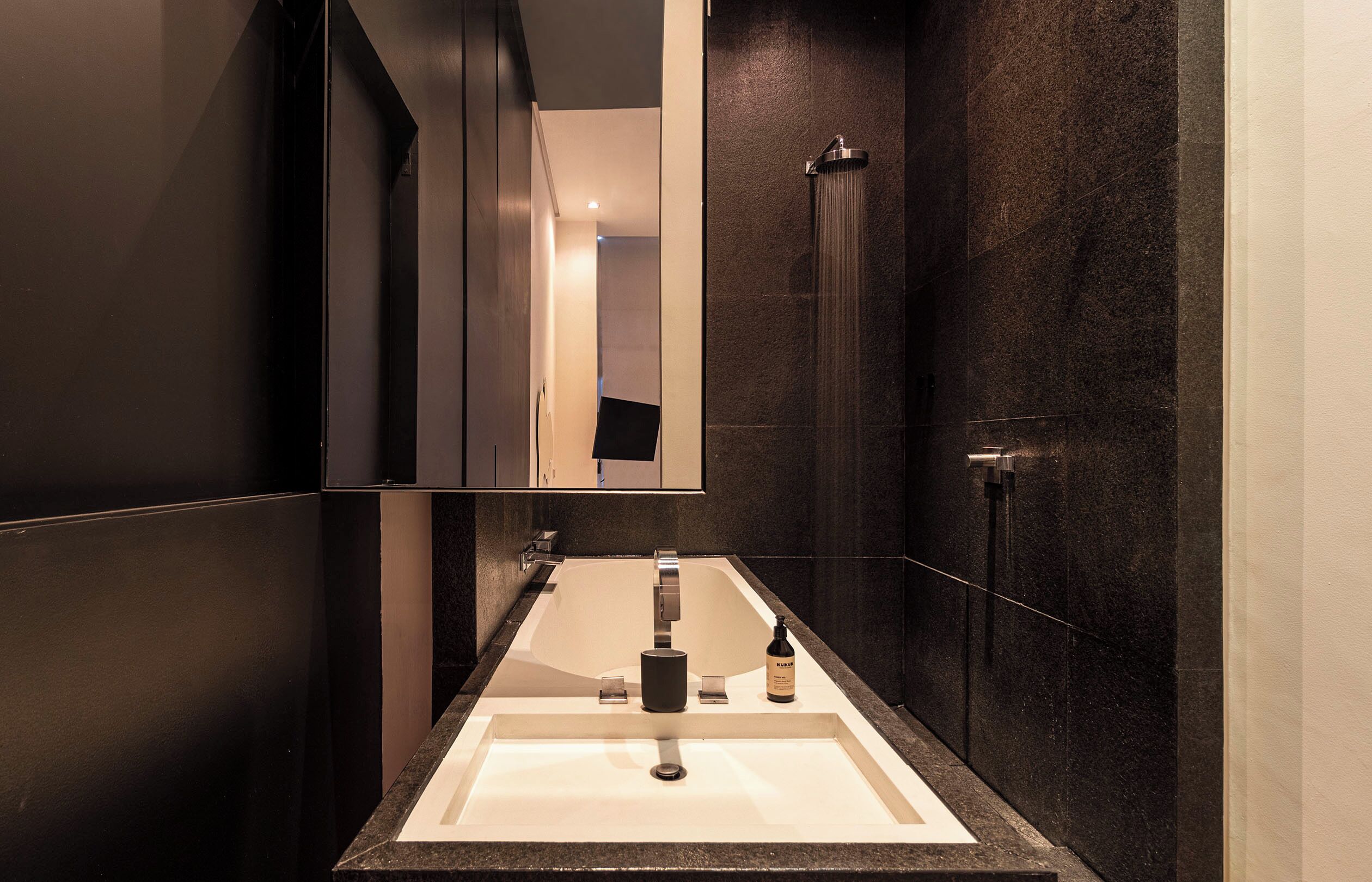 Un baño moderno con una pared oscura, un espejo grande, un lavamanos y una ducha.