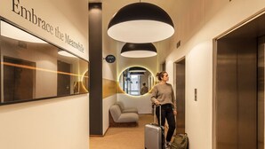 Un pasillo de hotel con un espejo grande, un cartel que dice 'Embrace the Moment' y una lámpara moderna.