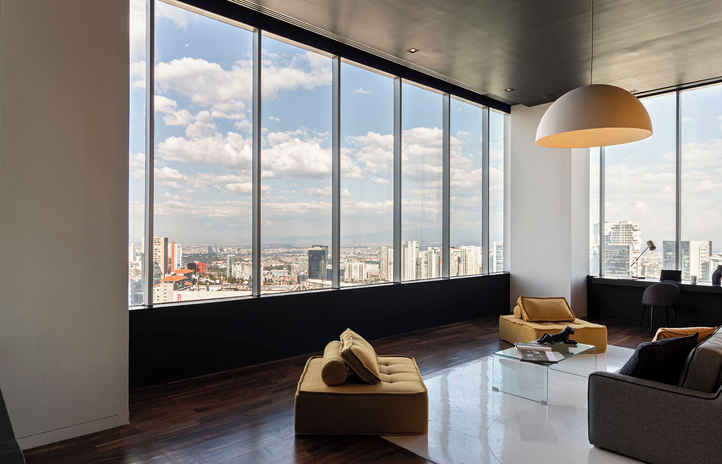 Un salon moderne avec une grande fenêtre, un canapé, une table basse et un luminaire suspendu.