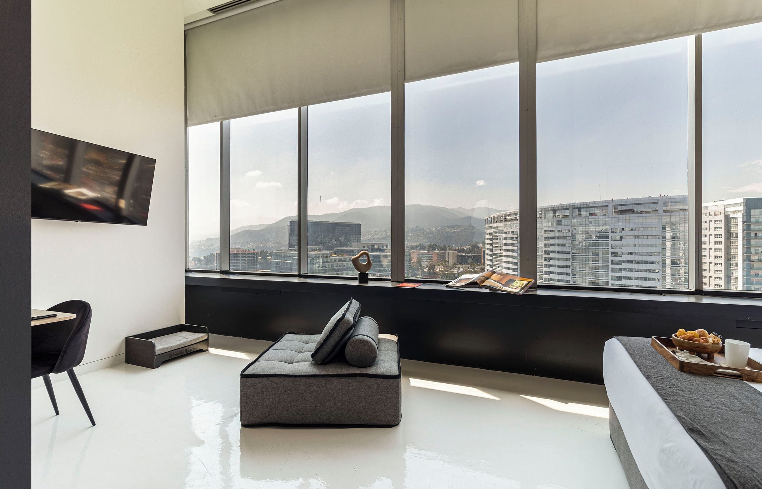 A modern living room with a large window, a flat-screen TV, a sofa, a coffee table, and a chair.