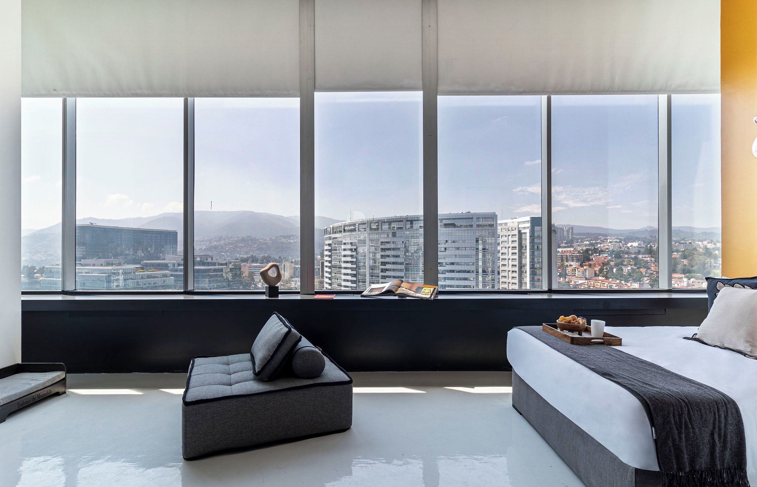Une chambre d’hôtel moderne dotée d’une grande fenêtre, d’un lit, d’un coin salon et offrant une vue sur le paysage urbain.