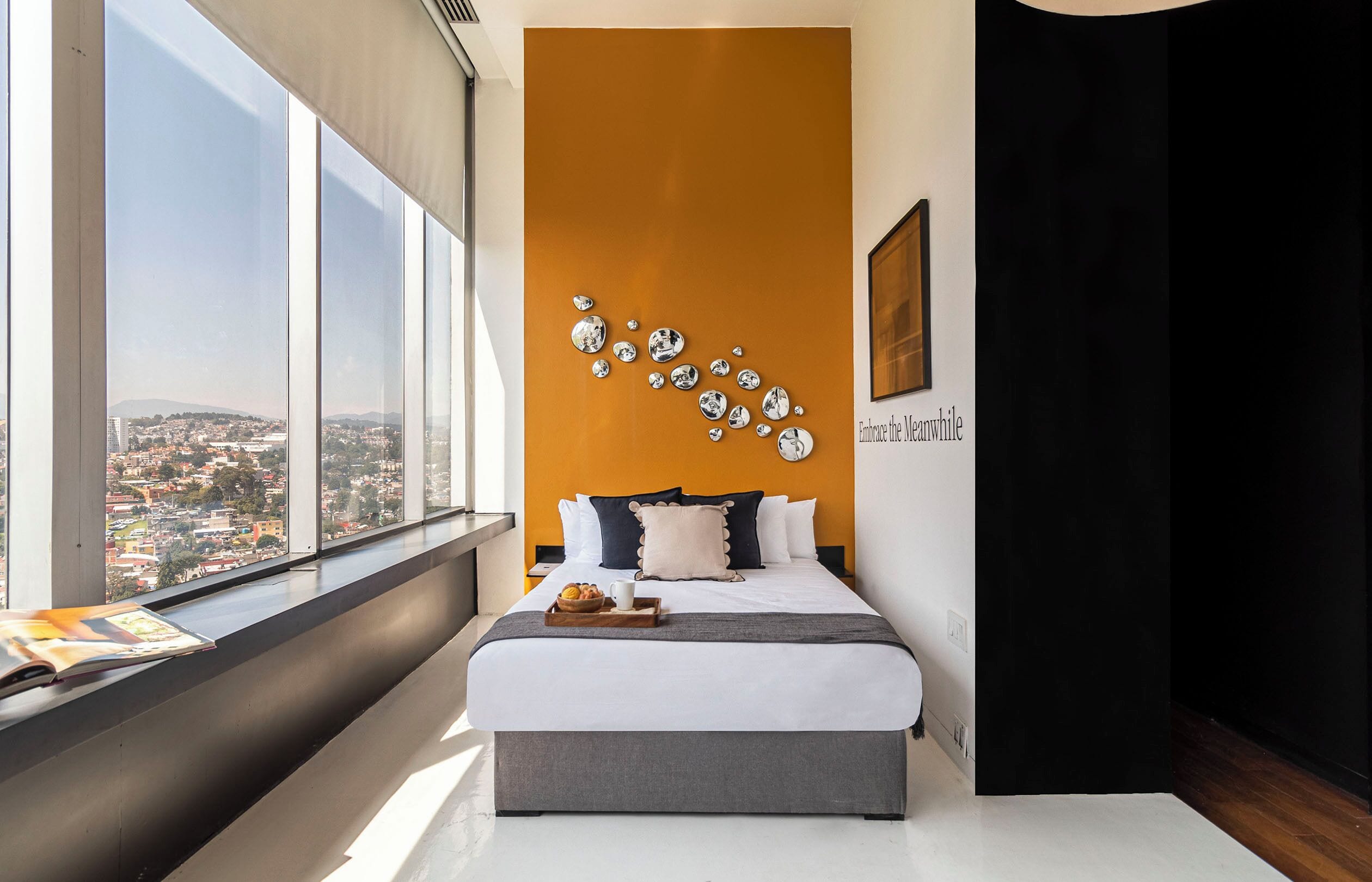 A modern bedroom with a large window, a bed with white bedding, and a city view.