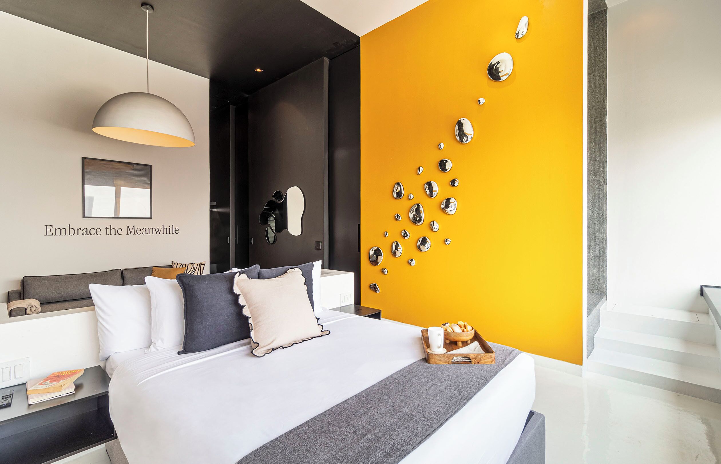 A modern bedroom with a bed, bedside tables, a wall-mounted mirror, and a yellow accent wall with decorative mirrors.