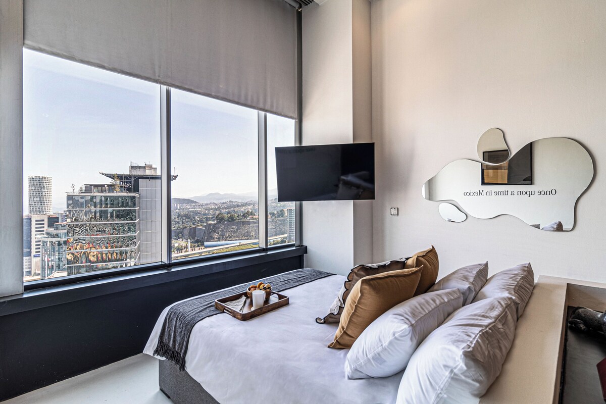 A modern hotel room with a large window, a flat-screen TV, a bed with pillows, and a tray with a cup and a book.