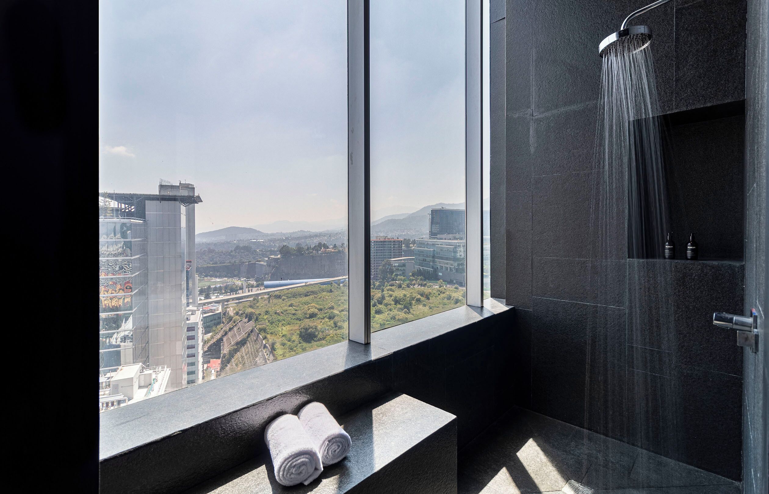 Un baño moderno con un ventanal grande, una ducha y dos toallas enrolladas en el alféizar.