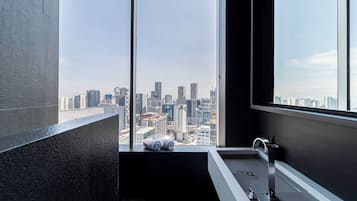 A modern bathroom with a large window, a bathtub, and a toilet.